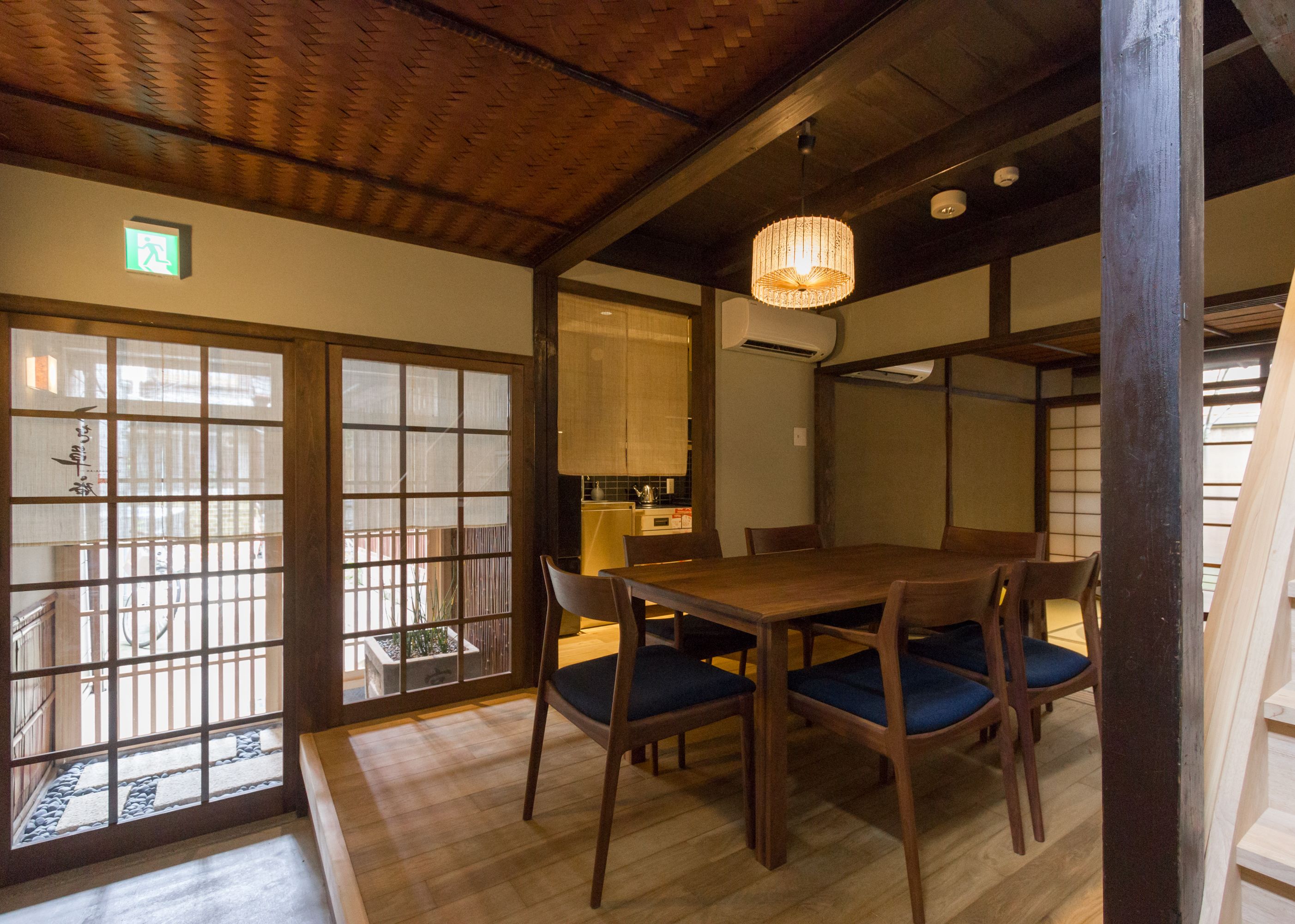 A traditional Japanese-style room with tatami flooring, a wooden dining table with blue cushions, and a sliding door with a view of the outside.