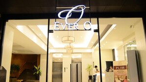 Der Eingang eines Hotels mit Glasfassade, einer Neonreklame und einem einsehbaren Empfangsbereich.