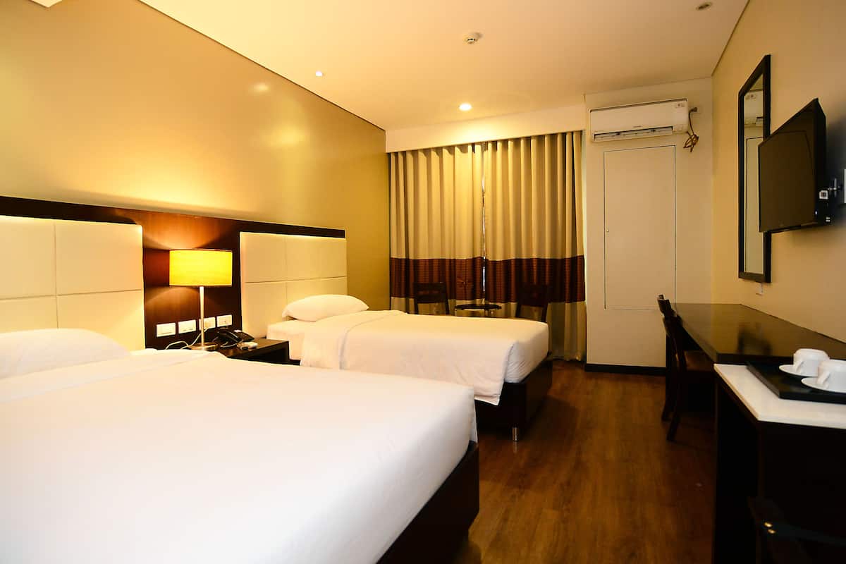 A hotel room with two beds, a desk, a chair, a lamp, a TV, and an air conditioning unit.