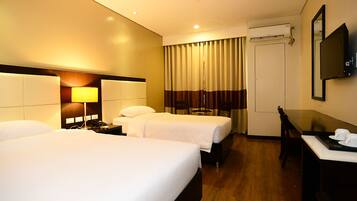 A hotel room with two beds, a desk, a chair, a lamp, a TV, and an air conditioning unit.