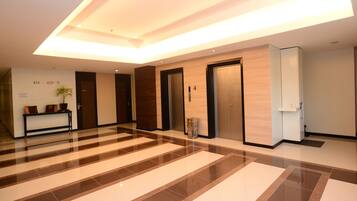 A modern hotel lobby with a check-in counter, reception desk, and a large, patterned floor.