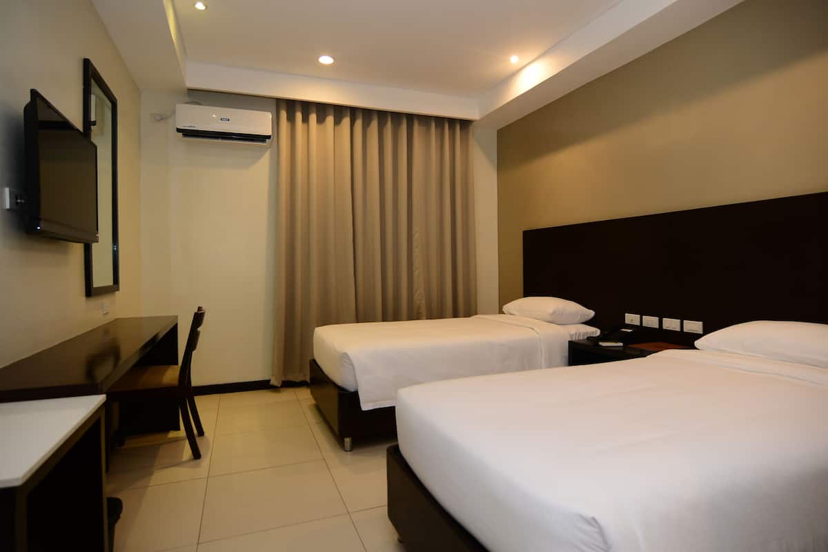 A hotel room with two single beds, a desk, a chair, a TV, and an air conditioning unit.