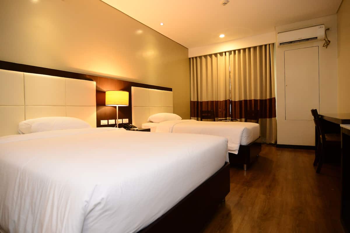 A hotel room with two beds, a desk, a lamp, and an air conditioning unit.