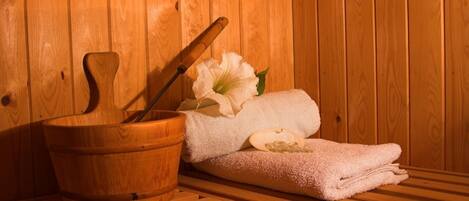 A wooden sauna with a wooden bucket, a wooden mallet, and a white towel with a flower.