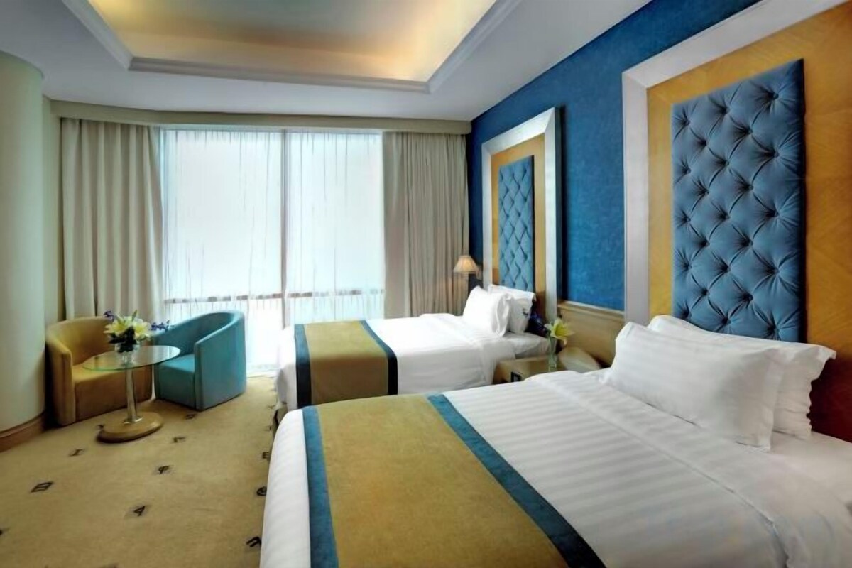 A hotel room with two beds, a sofa, a small table, and a large window.