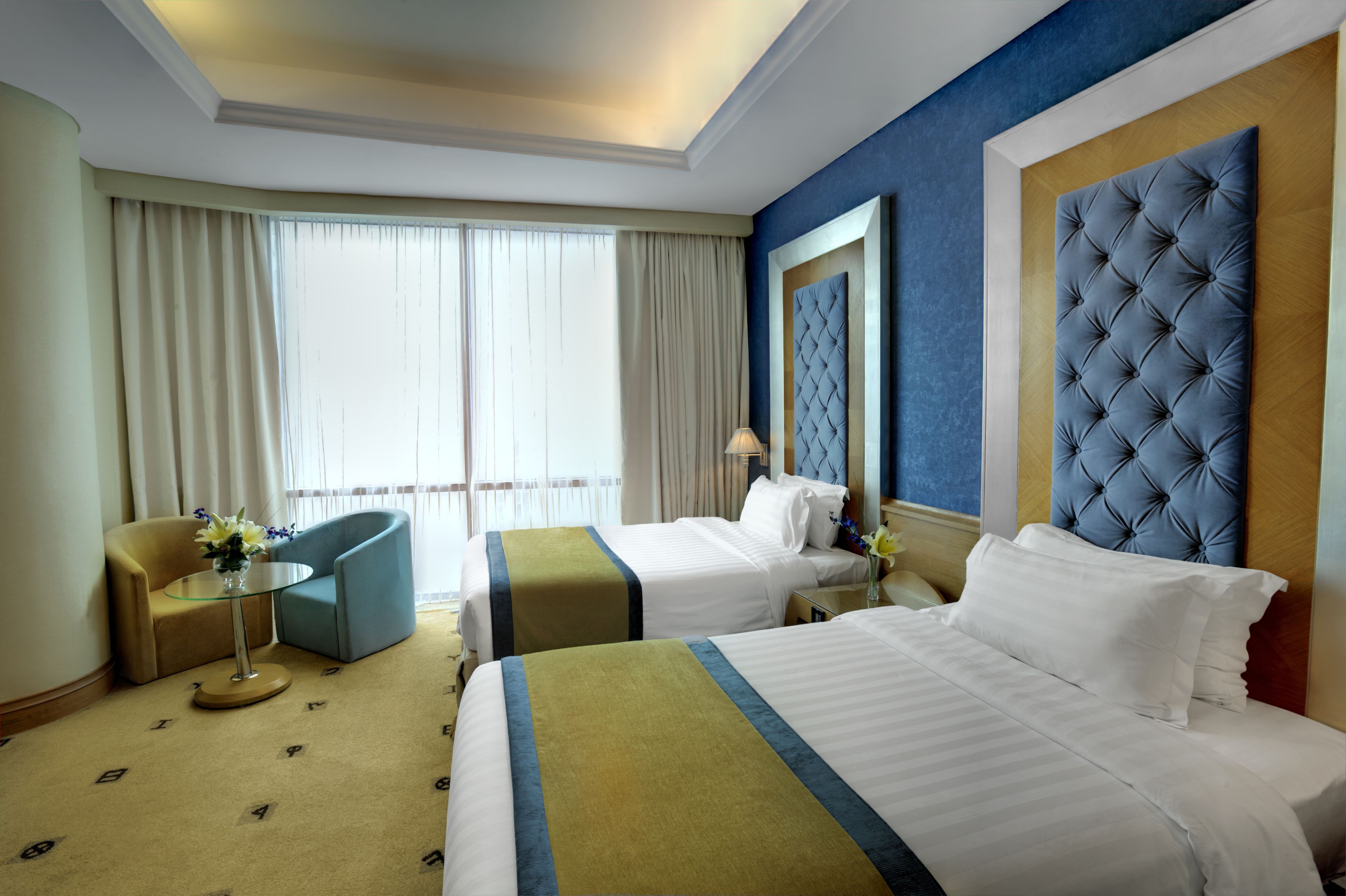 A hotel room with two beds, a sitting area with a chair and a small table, and a large window with curtains.