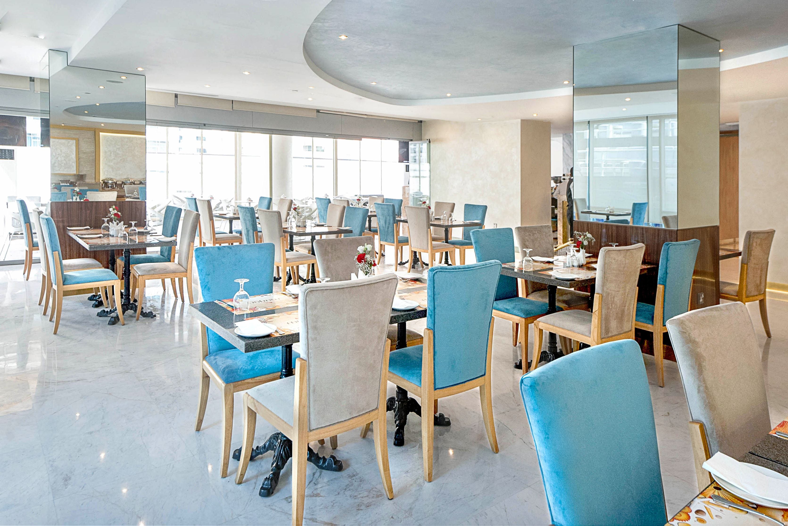 A spacious dining area with multiple tables and chairs, large windows, and a modern interior design.