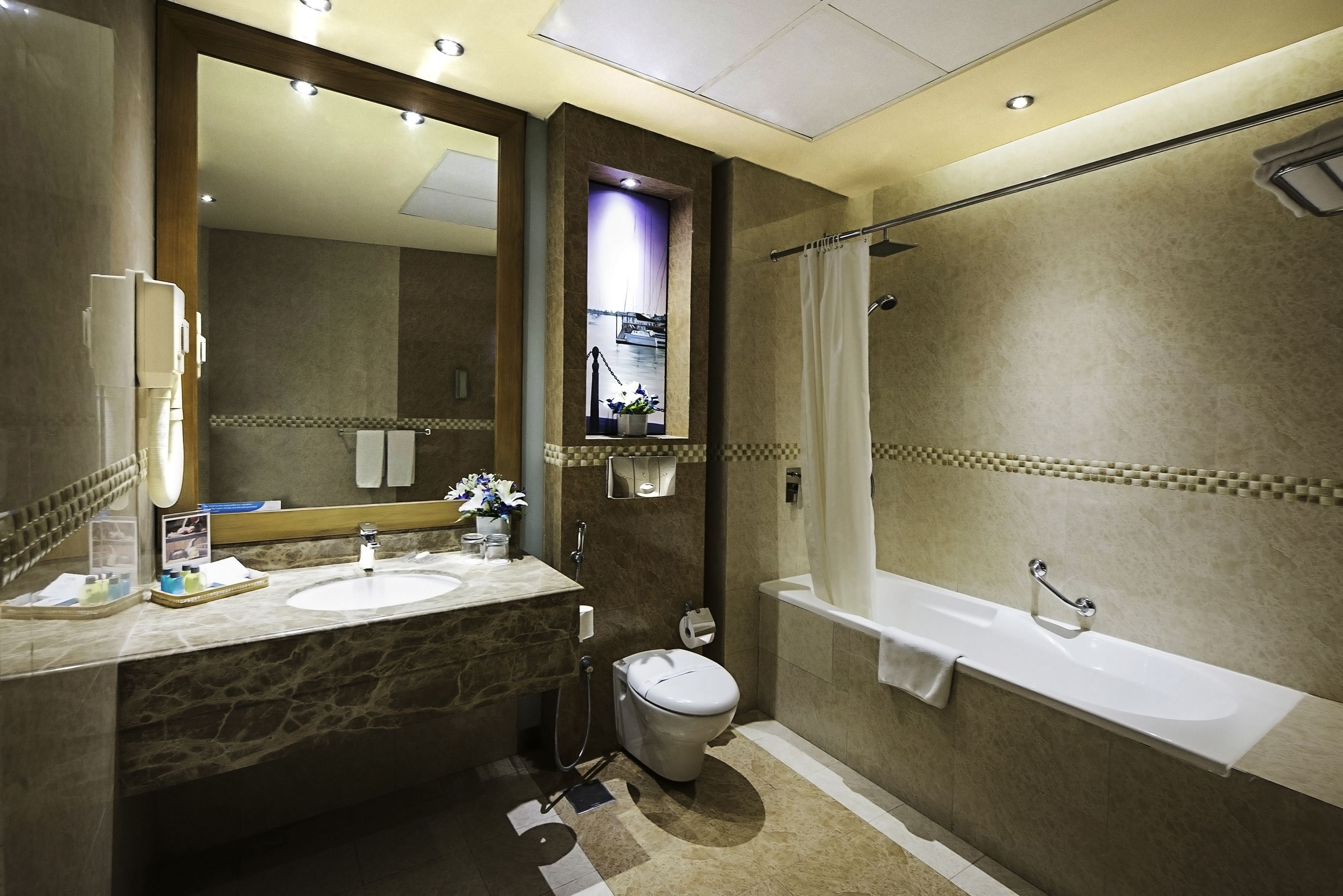 Een badkamer met een marmeren wastafel, een grote spiegel, een toilet, een bad en een douchegordijn.