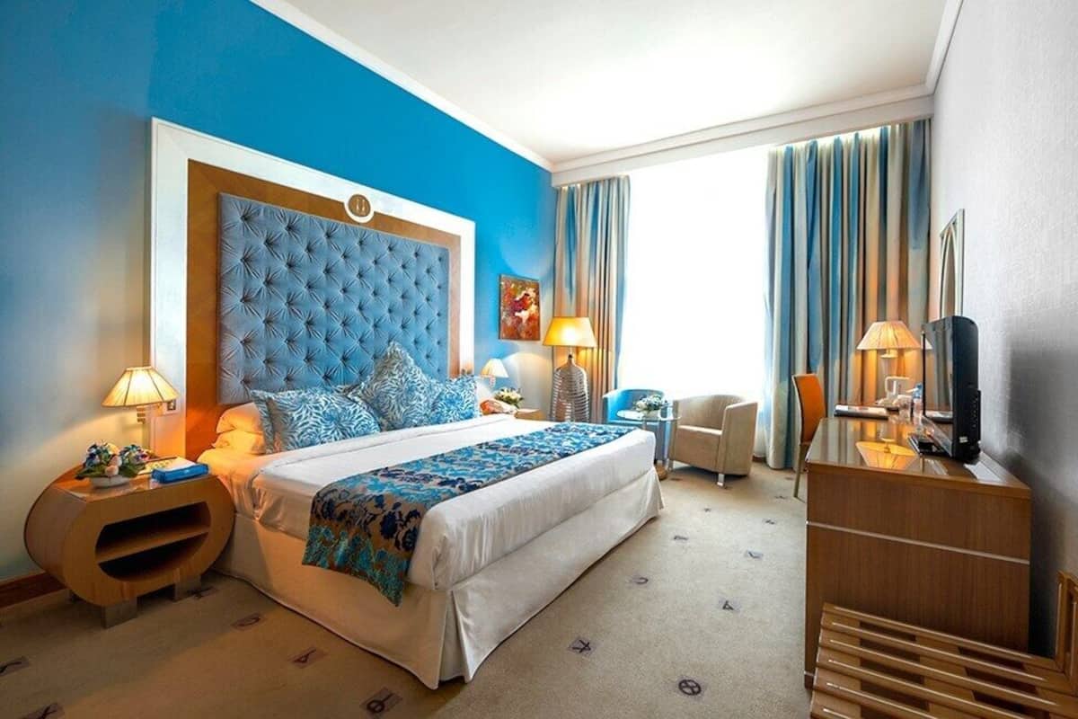 A hotel room with a large bed, a wooden dresser, a desk, and a TV.