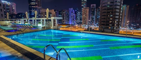Ein Schwimmbad mit gefliestem Deck und Blick auf die nächtliche Stadtlandschaft.