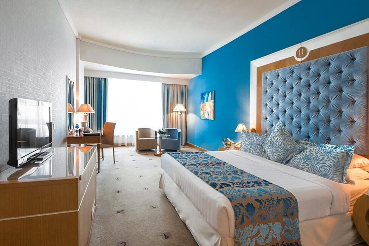 A hotel room with a large bed, a TV, a desk, and a chair.