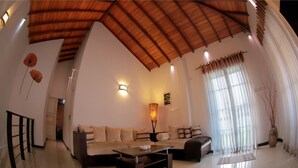 A spacious living room with a high ceiling, a sofa set, a coffee table, and a large window with sheer curtains. - Blue Water Boutique Hotel (Negombo)