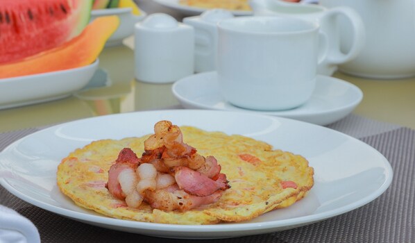 Un plato con una tortilla cubierta de tocino y cebollas, una taza blanca y una rebanada de sandía al fondo.