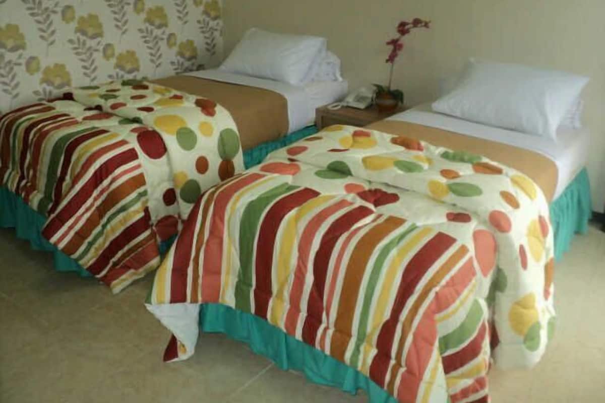 A hotel room with two beds, each with a colorful striped bedspread and white pillows.