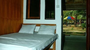 Un dormitorio con cama, paredes de madera y vista a un espacio exterior con palmeras y un paraguas azul.