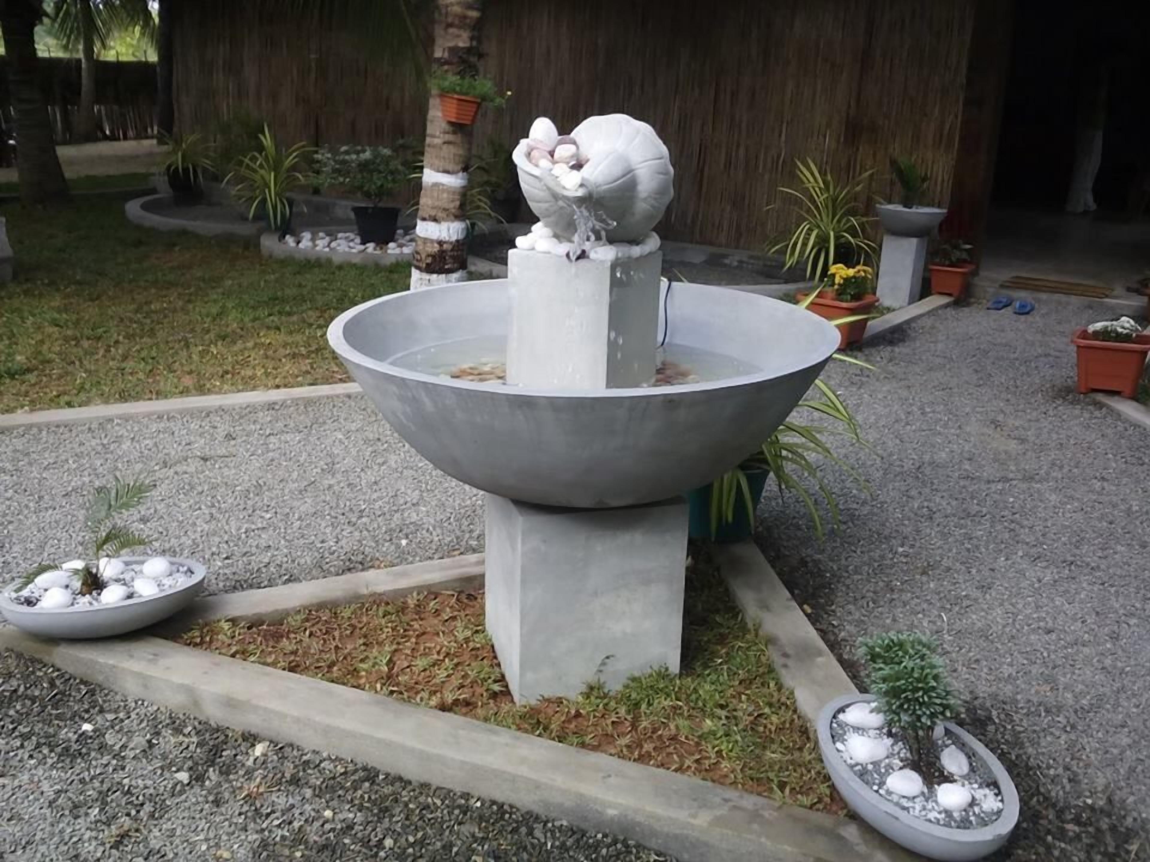 Un jardin agrémenté d’un élément aquatique central, entouré de plantes en pot et bordé d’un chemin de gravier.