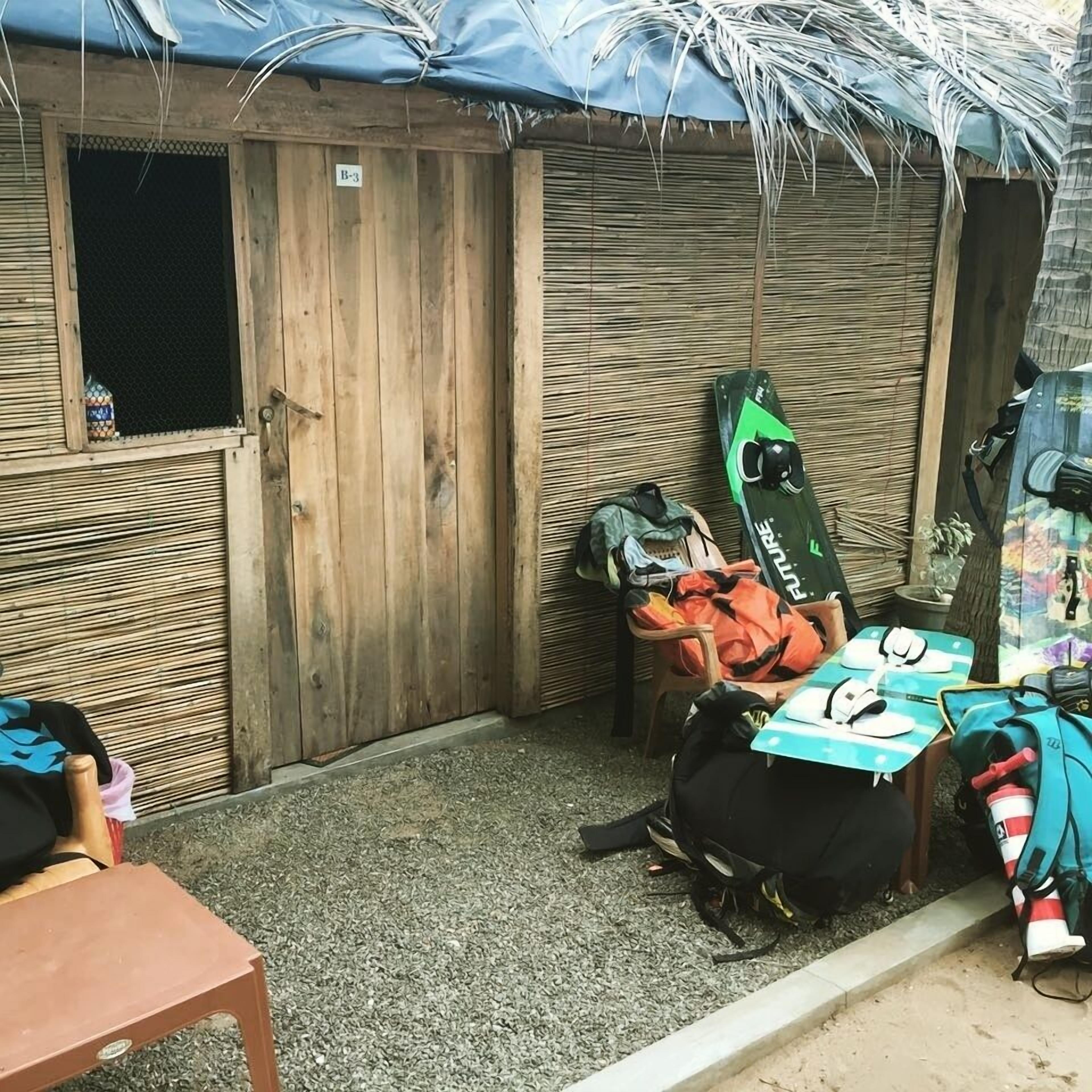 Un petit espace extérieur clos, doté d’une porte en bois, d’une table, ainsi que de divers sacs et équipements.