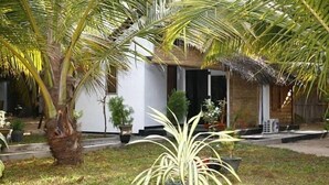 Una casa con techo de paja, rodeada de palmeras y plantas en macetas.