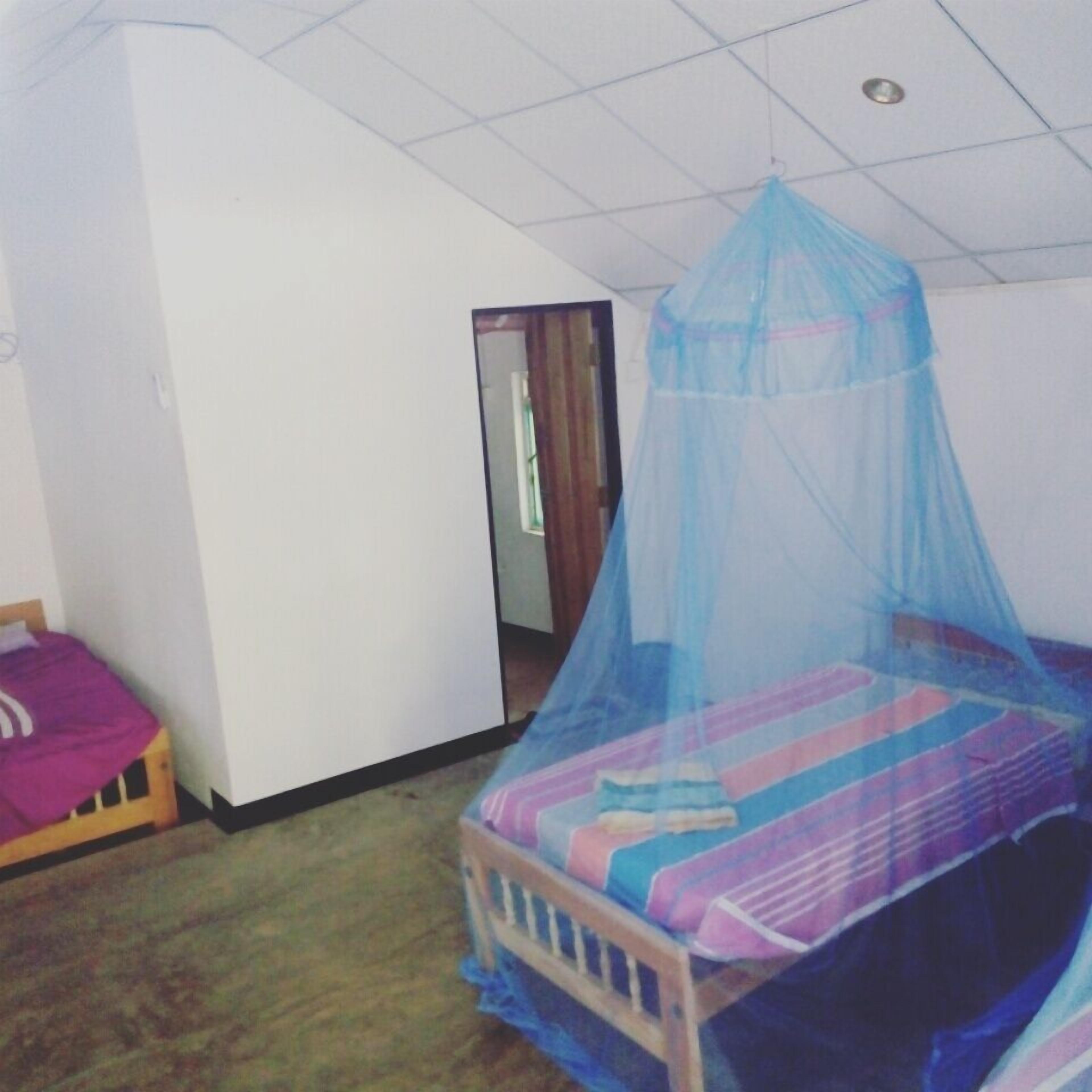 Une chambre à coucher avec un lit recouvert d’une moustiquaire, une tête de lit en bois et une petite table de chevet recouverte d’un tissu violet.