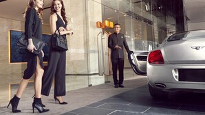 A modern hotel entrance with a glass facade, a silver car parked outside, and a person standing by the entrance. - THE FACE Suites Hotel (Kuala Lumpur)