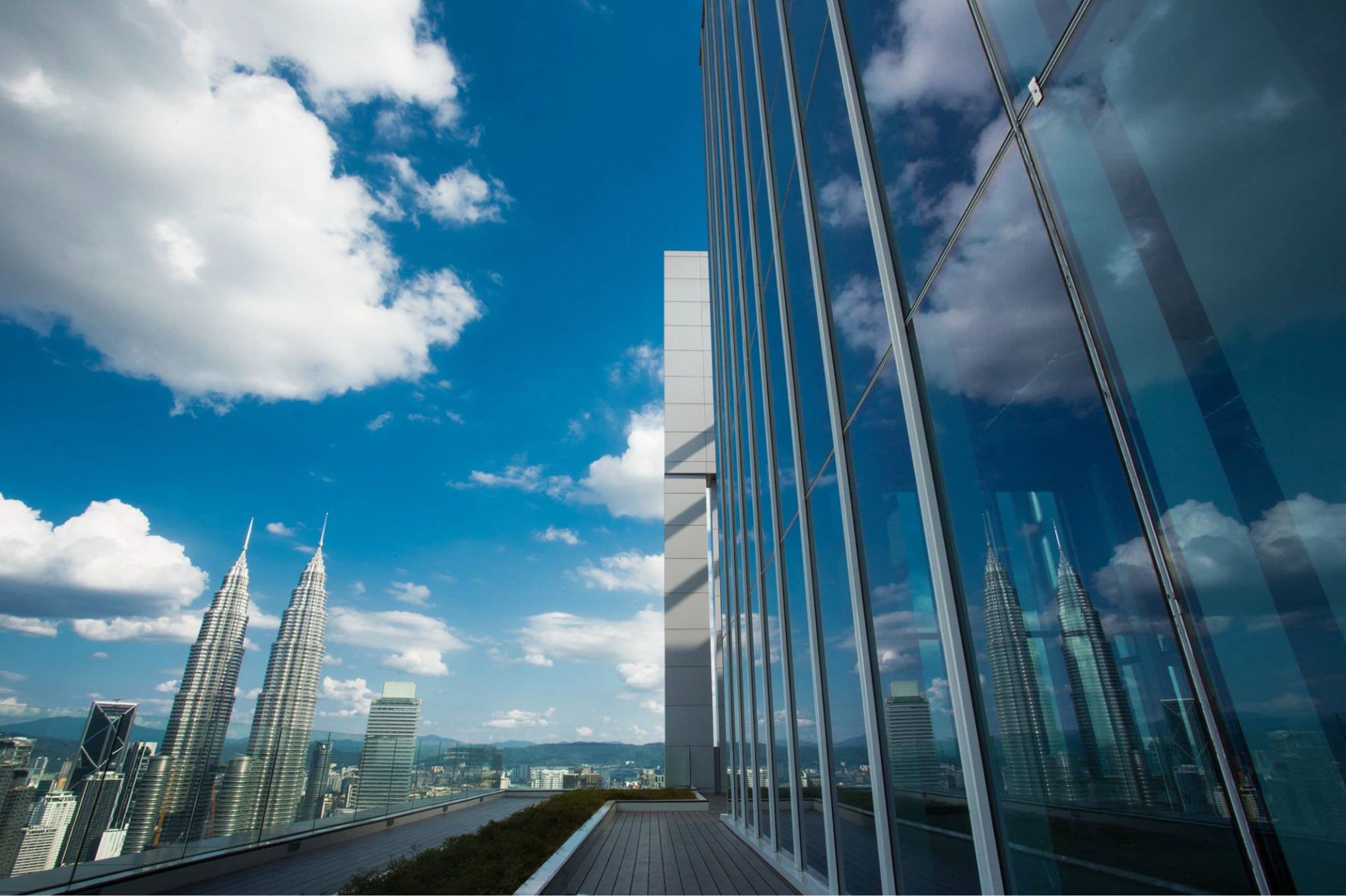 Un edificio moderno con amplios ventanales que reflejan el cielo y rascacielos cercanos.