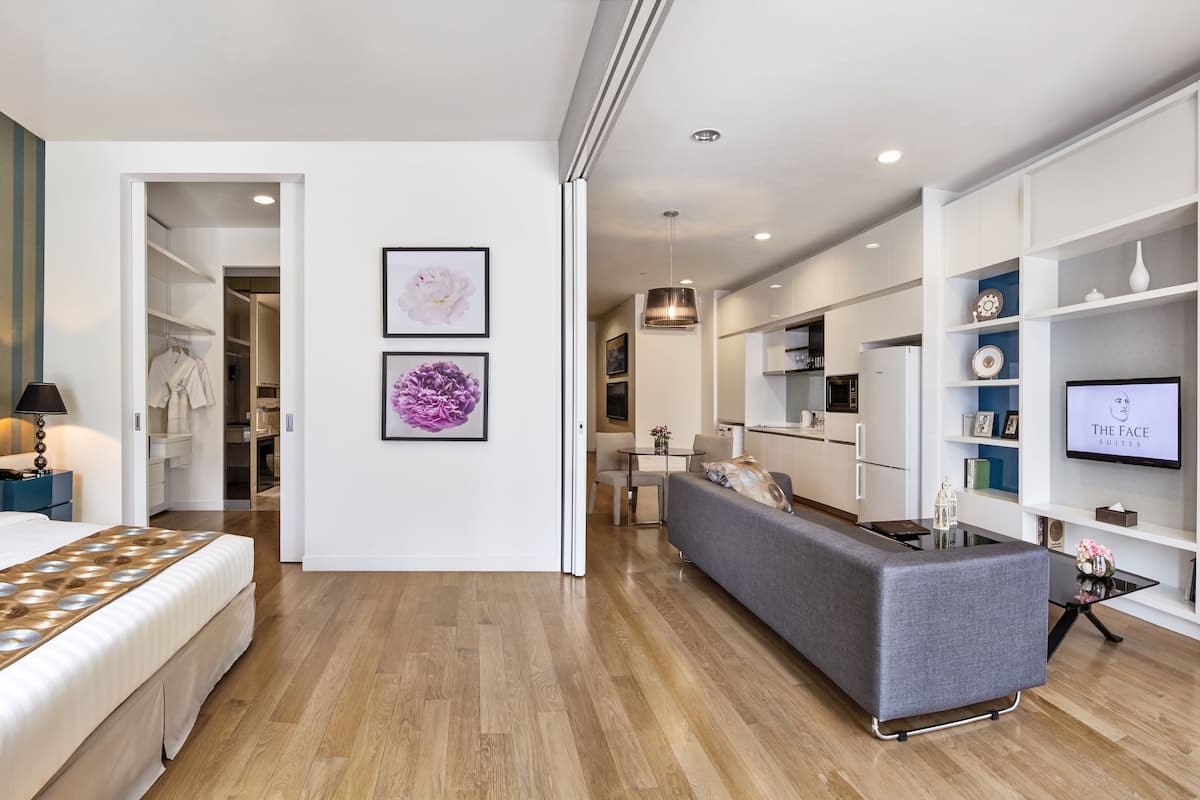 A modern hotel room with a bed, a sofa, a dining area, and a TV.