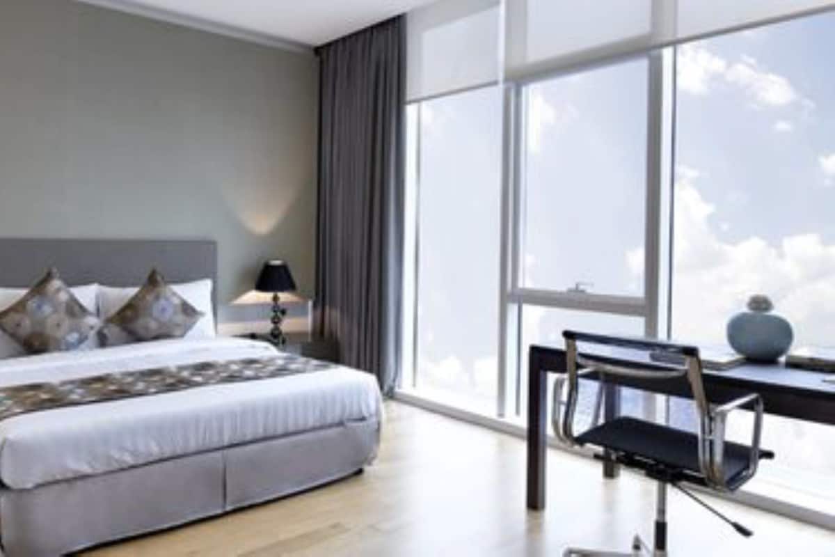 A modern hotel room with a large bed, two bedside tables with lamps, a desk with a chair, and a large window offering a view of the sky.