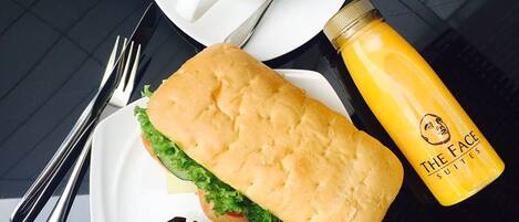 Una comida que incluye un sándwich, un muffin, una taza de café con arte latte y una botella de jugo sobre una mesa.