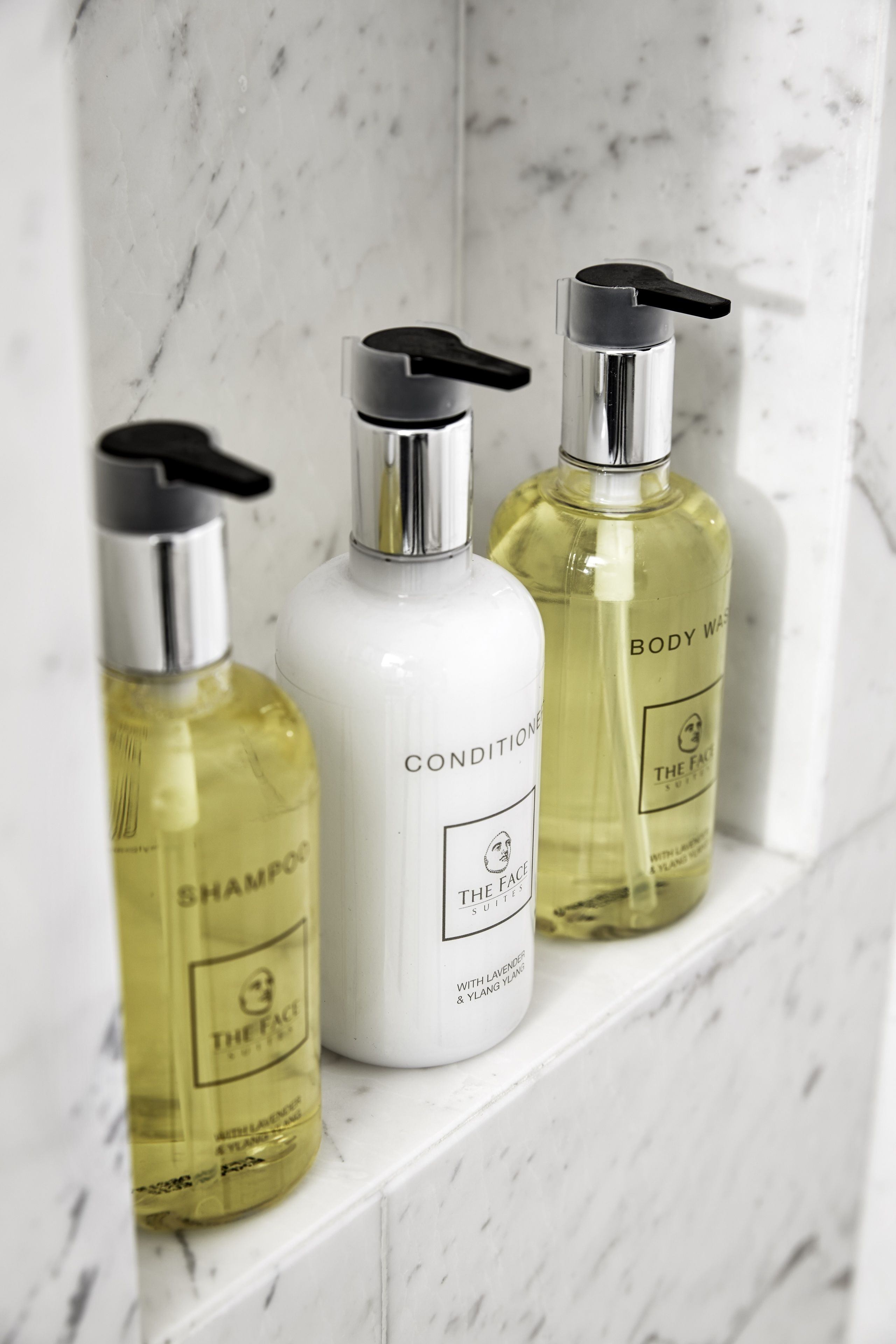 Tres botellas de crema limpiadora y acondicionador para el cuerpo de la marca The Face sobre un estante de mármol.