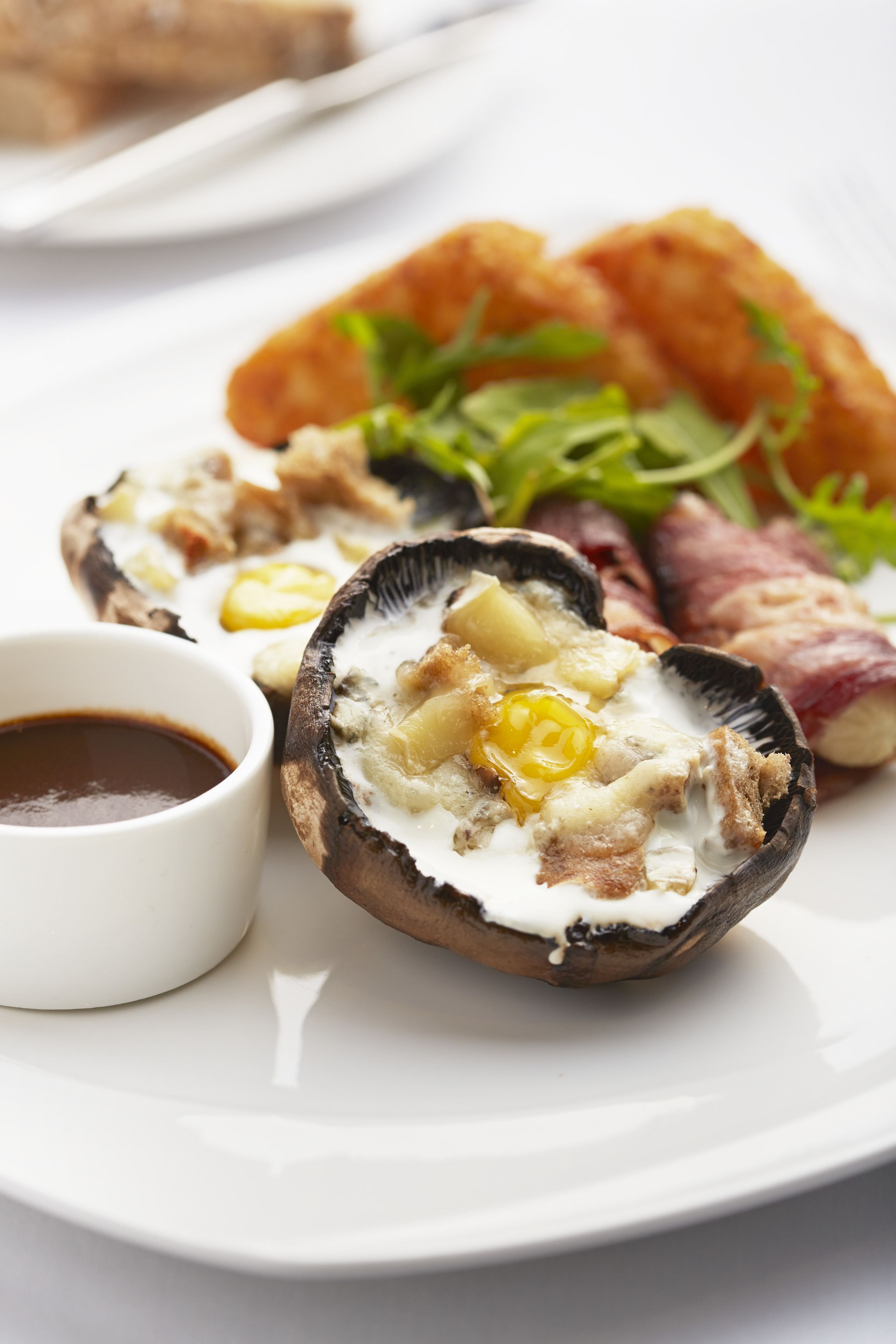 A plate with a stuffed mushroom, a small bowl of sauce, and some greens.