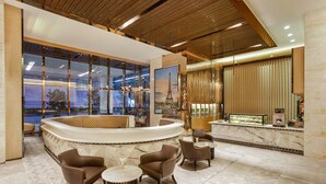 A modern lobby with a curved reception desk, seating area, and large windows overlooking a pool. - THE FACE Suites Hotel (Kuala Lumpur)