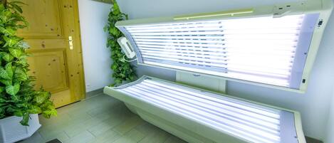 A room with two tanning beds, a wooden door, a scale, and a potted plant.