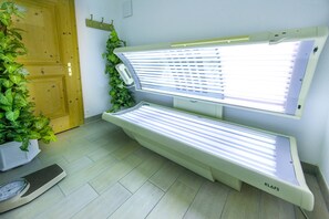 Ein Raum mit zwei Solarien, einer Holztür, einer Waage und einem Blumentopf.