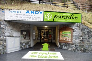 A hotel entrance with stone walls, a sign for 'Haus Andy' and 'Zermatt Paradies' accommodations, and an arrow indicating the tunnel entrance.