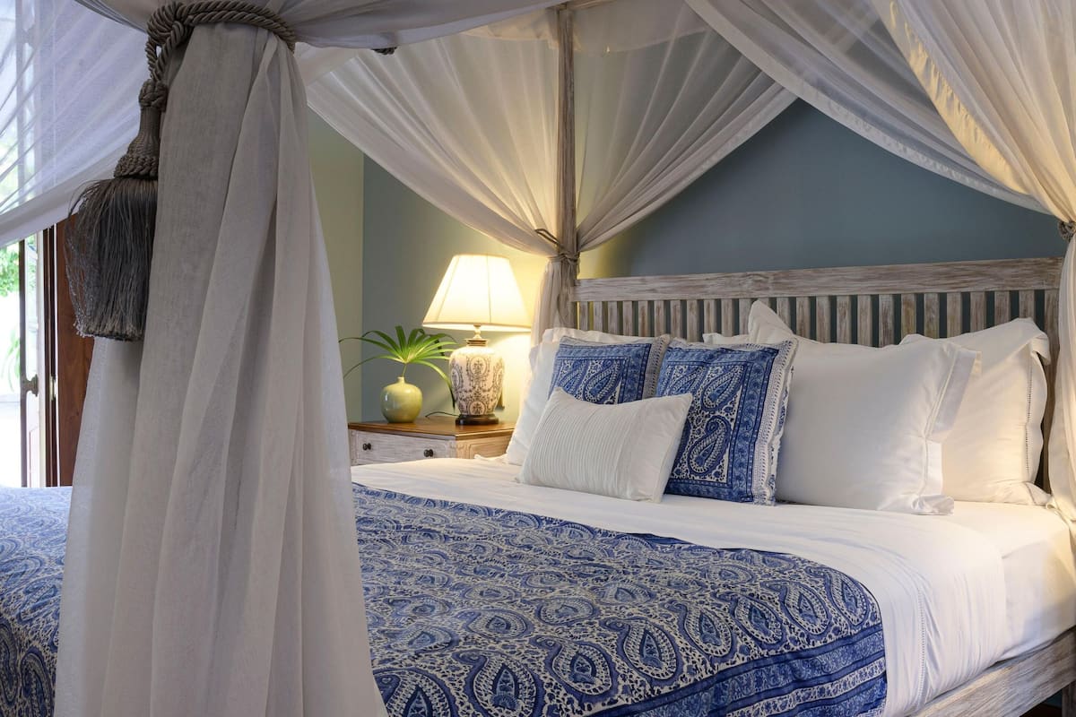 Un dormitorio con cama con dosel, dos lámparas de noche y una mesita de noche con un florero.