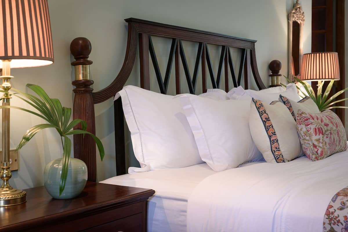 Una cama bien hecha con sábanas blancas y almohadones decorativos, un cabecero de madera y dos lámparas de noche.