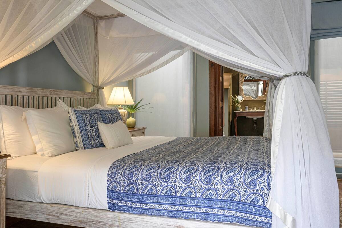 Una cama con dosel, dos lámparas de noche y un jarrón decorativo en la mesita de noche.