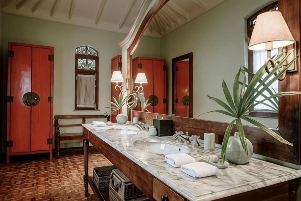 A bathroom with two sinks, a large mirror, a bench, and a potted plant.