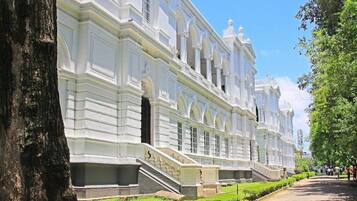 A large, white, multi-story building with a symmetrical facade, large windows, and a central staircase leading to the entrance.