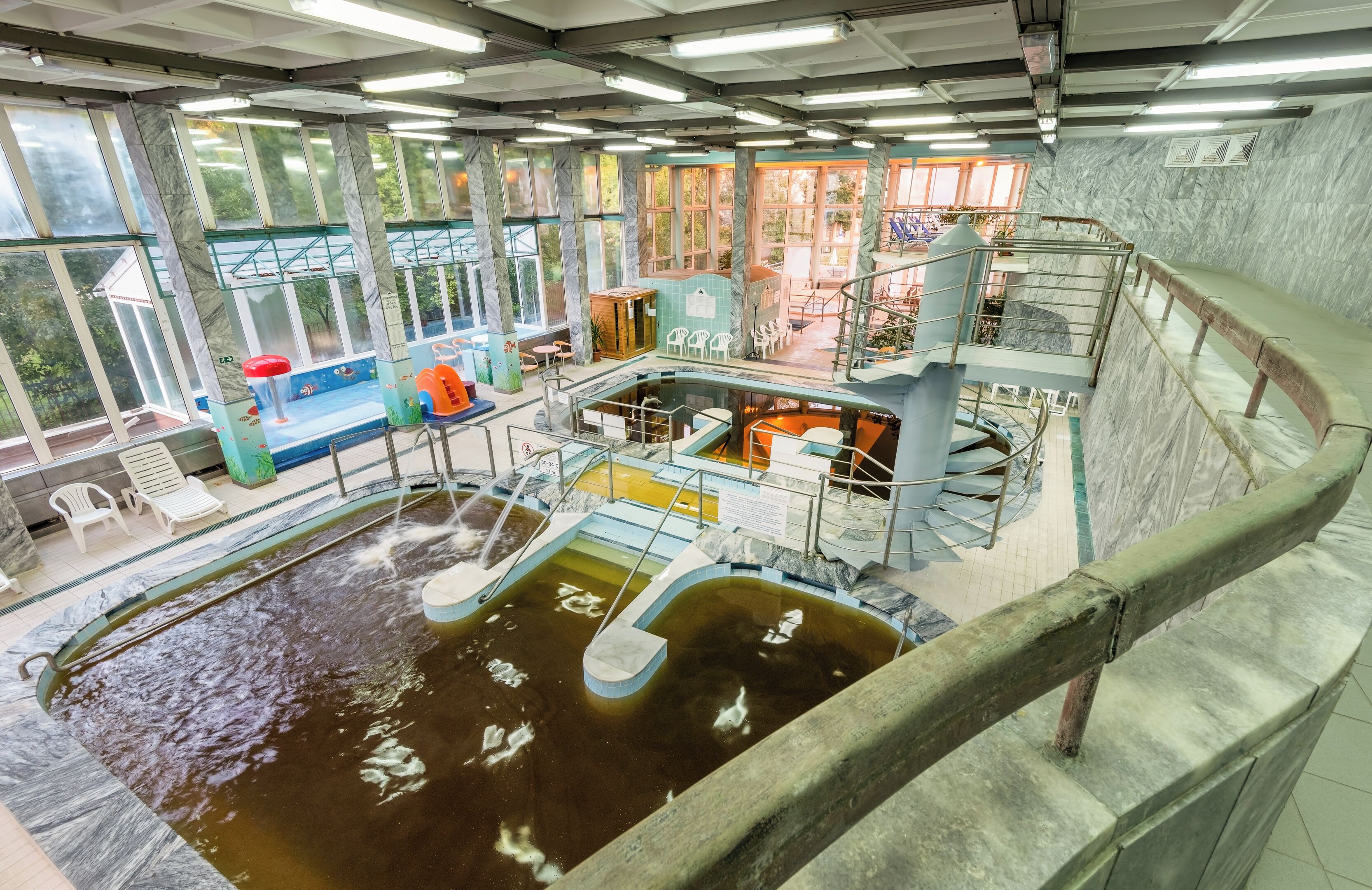 Una piscina interior de varios niveles con diferentes zonas de estar y un elemento central de agua.