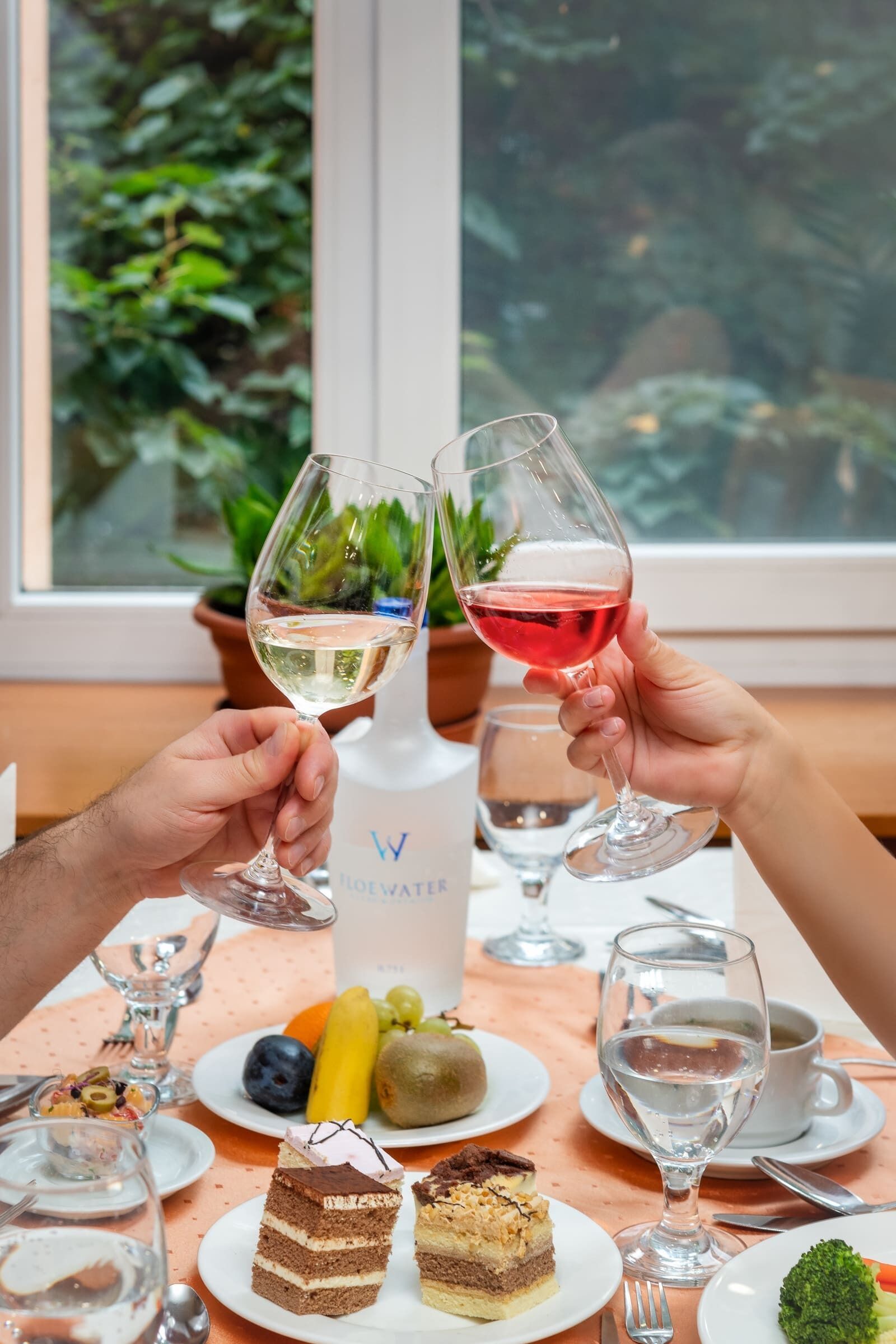 A table set with various dishes, including cakes and fruits, and two glasses of wine.