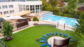 A swimming pool with lounge chairs, a covered seating area, and a building with large windows.