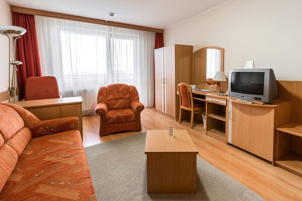 Quarto de hotel com sofá, poltrona, escrivaninha, televisão e guarda-roupa.