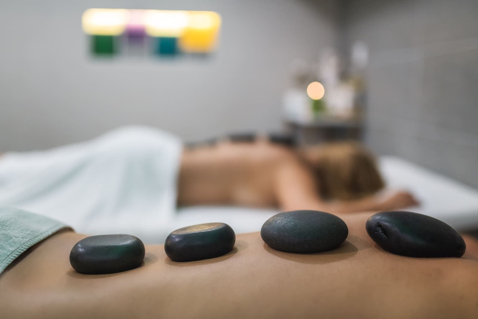 Uma sala de massagem com uma pessoa deitada numa cama recebendo uma massagem com pedras.