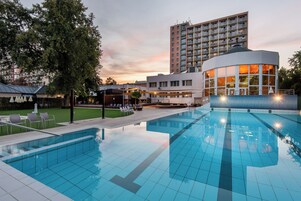 Una piscina con sillones de descanso, un pabellón y un edificio alto al fondo.