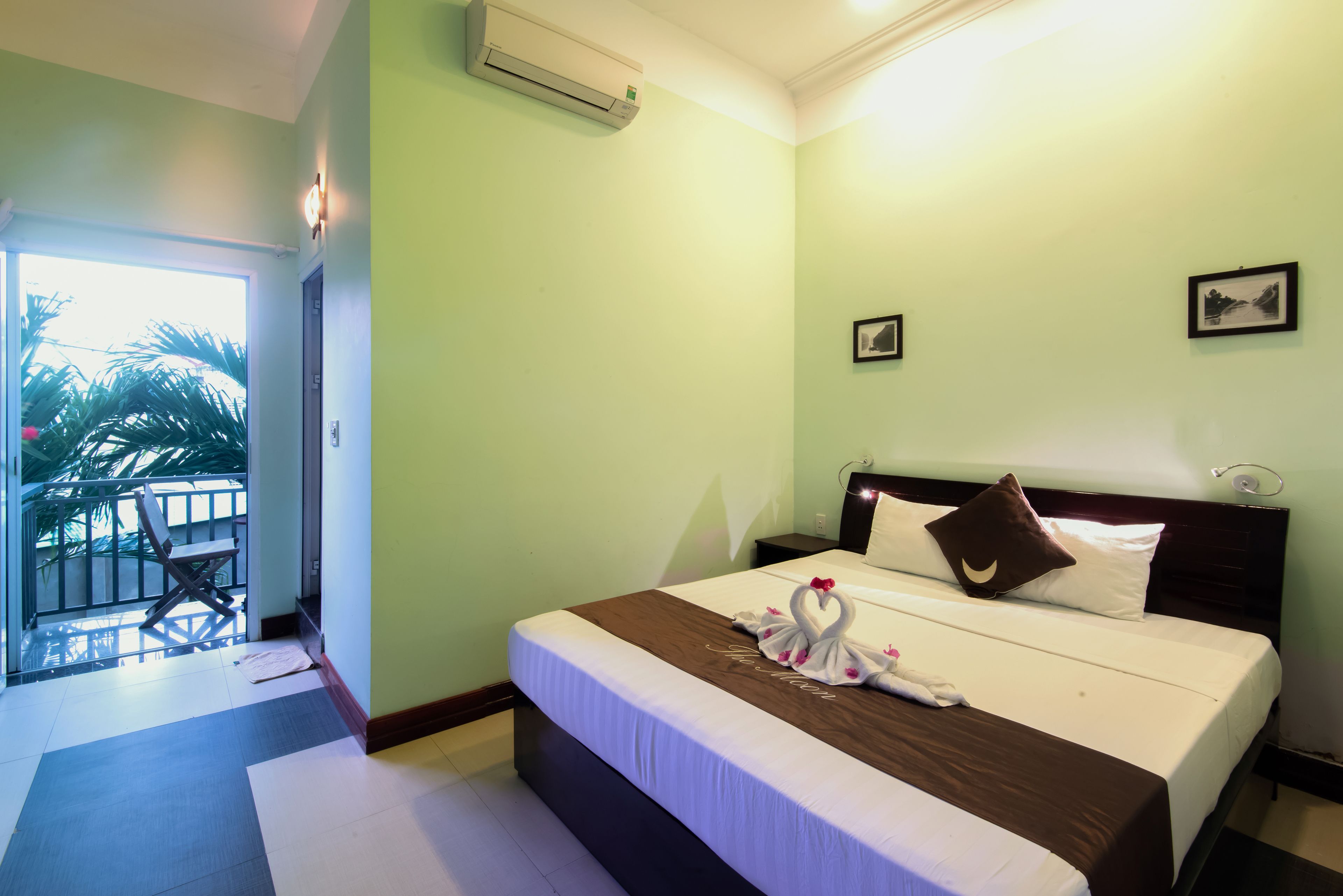 A hotel room with a bed, a balcony, and a view of palm trees.