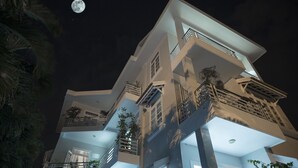 Un immeuble moderne à plusieurs étages, doté de balcons, de grandes fenêtres et où l’on aperçoit la lune dans le ciel.