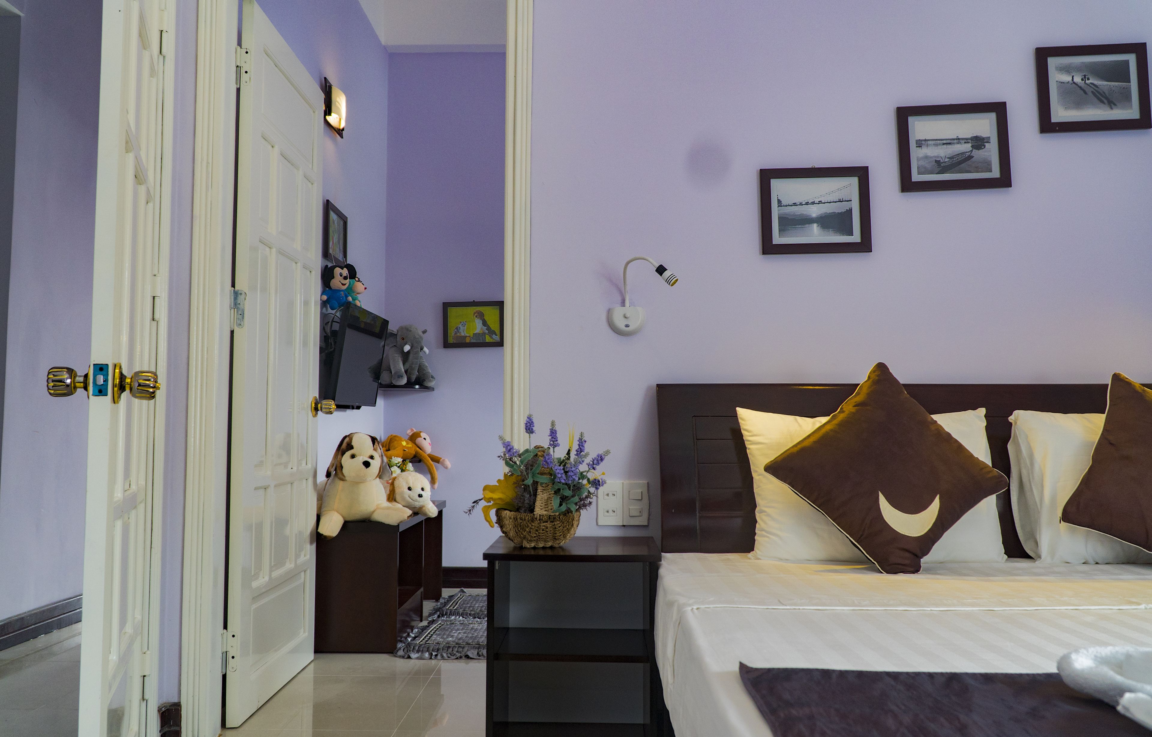 A bedroom with a bed, a nightstand, a lamp, and a wall with framed pictures.