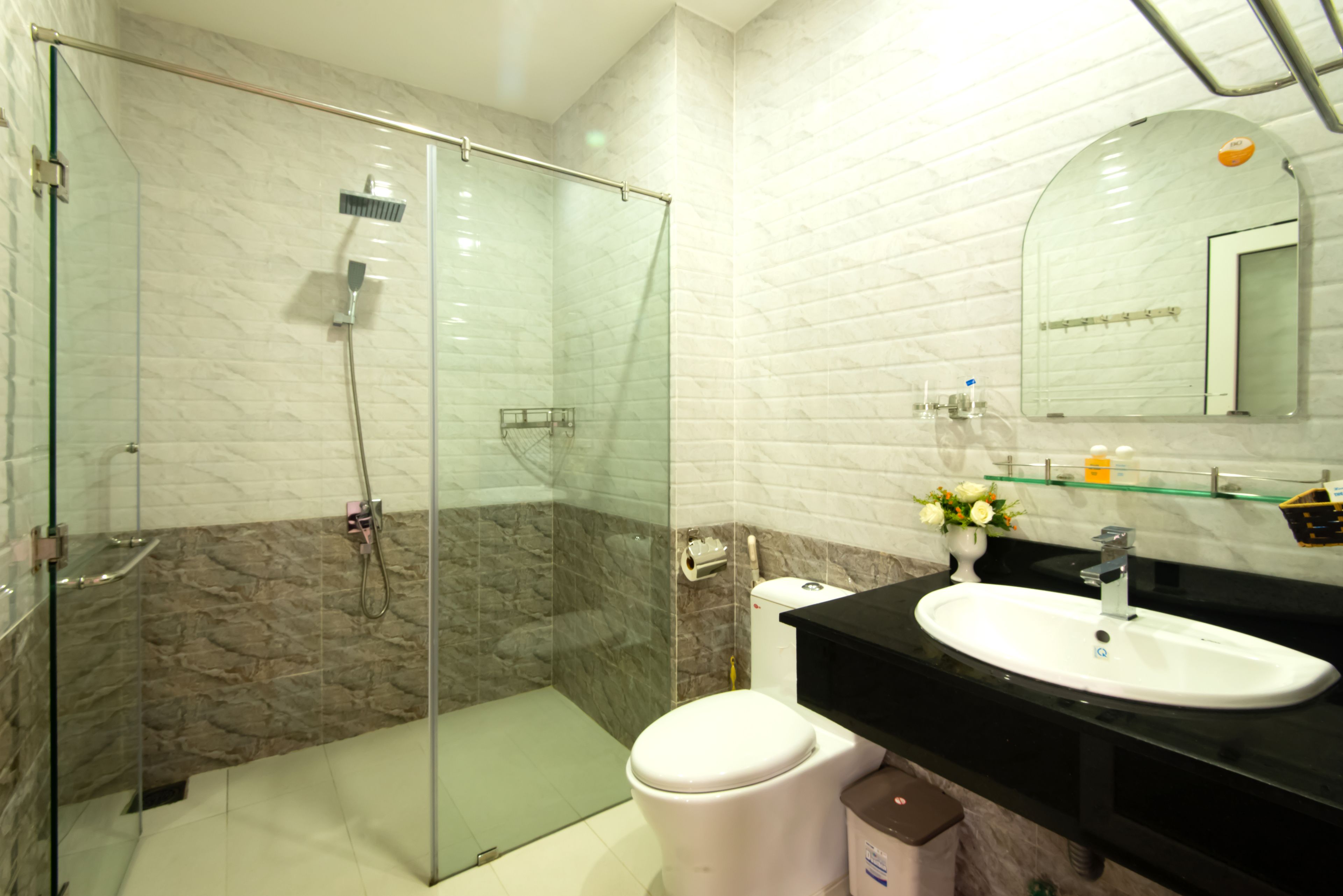 Ein modernes Badezimmer mit einer gläsernen Duschkabine, einer weißen Toilette, einem schwarzen Waschbecken und einer Wand mit Marmorfliesen.