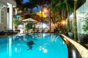 Una piscina interior con una escultura de delfín, rodeada de palmeras y una zona de estar cubierta.